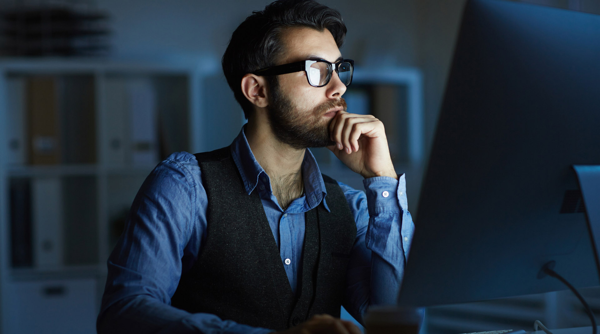A man in a dark room stares into a computer screen