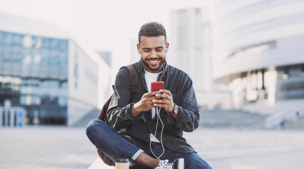 A young man looks into his cell phone while seated on a bench in the center of a public area