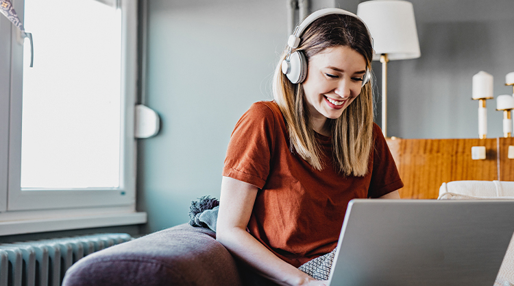 A smiling woman typing on her laptop while sitting in her living room