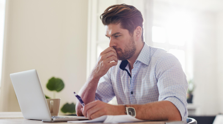 A man with a concerned expression seated in his home with his laptop open in front of him