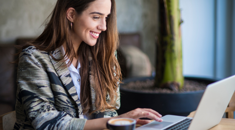 A smiling woman working on her laptop while seated at a desk
