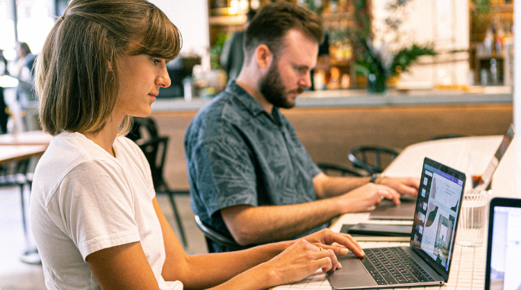 A woman working on her laptop in a restaurant next to another man also working