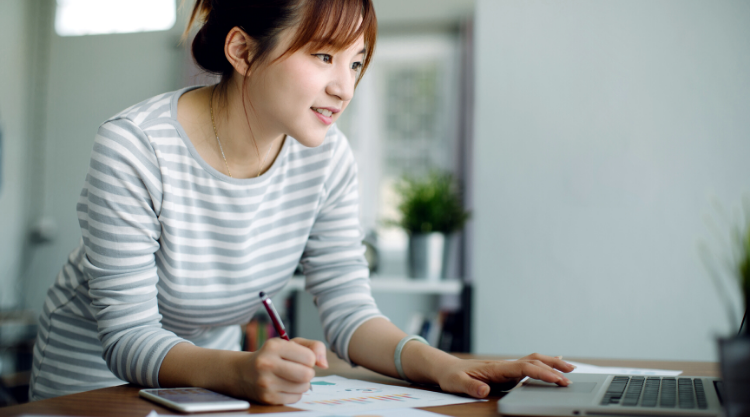 A young woman working on her laptop and taking notes in her living room