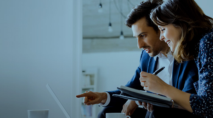 Woman writing in notebook with man pointing at laptop