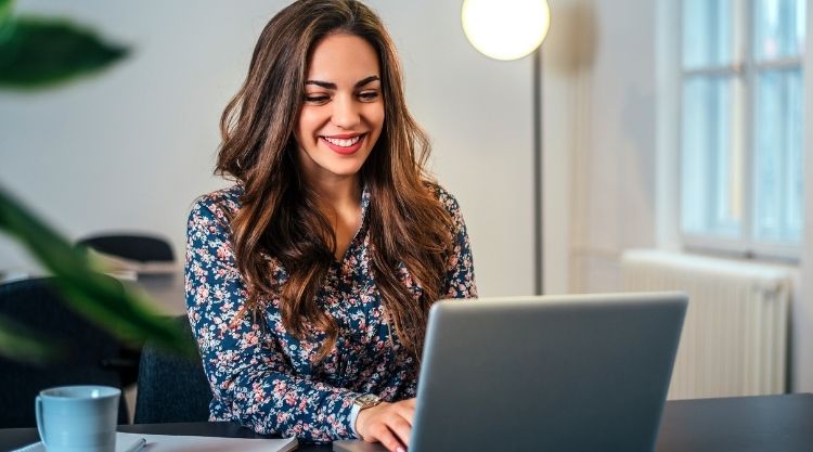 A smiling woman working on her laptop in her home