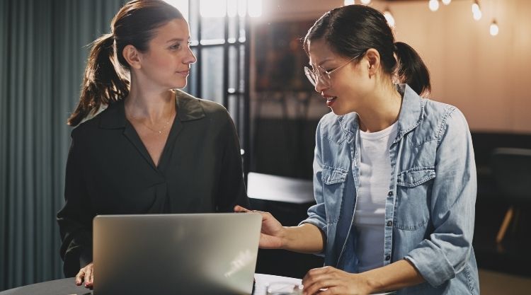 Two women talking at a restaurant while working on their laptop