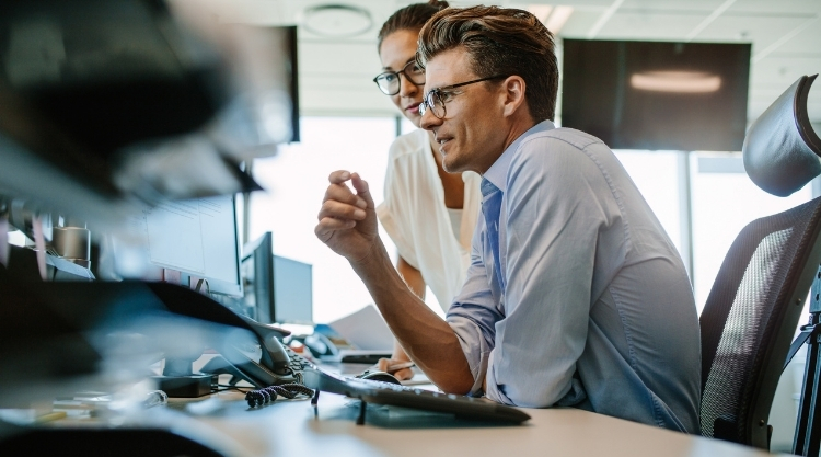 An adult man and woman in an office looking at the computer screen.