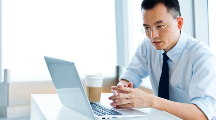 An adult man working on his laptop with a cup of coffee next to him