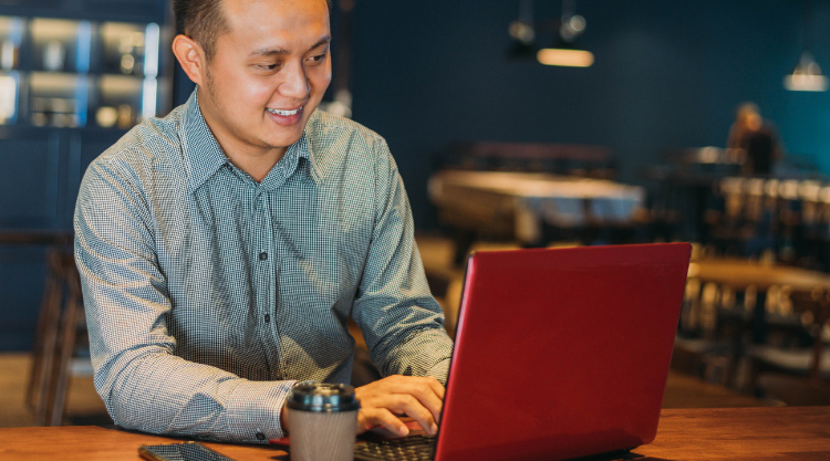 A man sitting at a table in a restaurant while working on his laptop