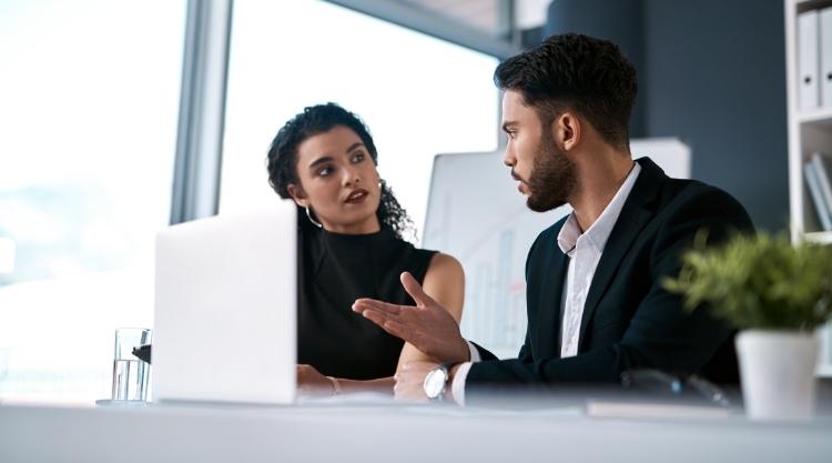 Cropped shot of two young businesspeople sitting together and having a discussion while using a laptop in the office