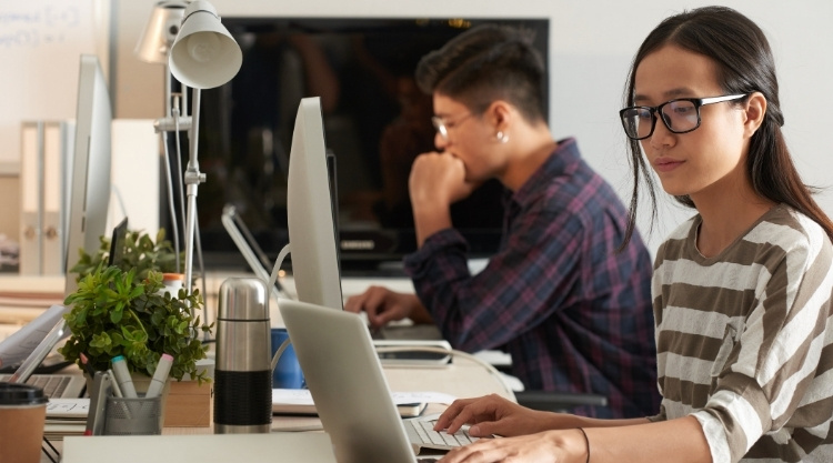 A woman sitting at her laptop working diligently while a coworker sits next to her in an office