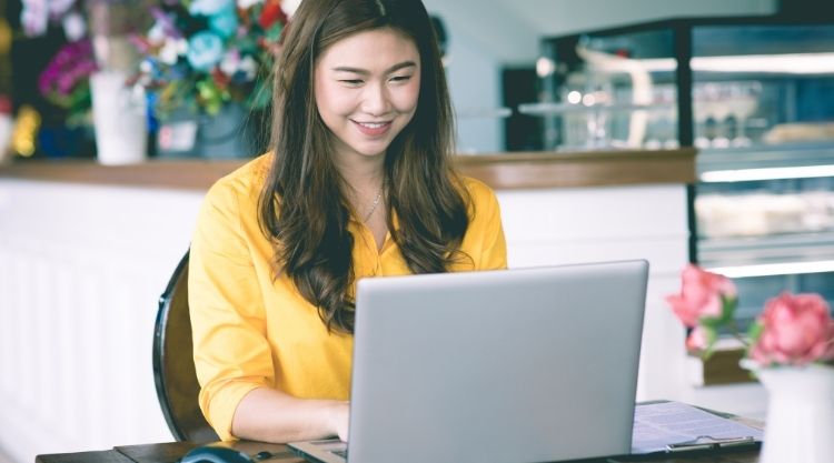 A smiling woman typing on her laptop in a cafe