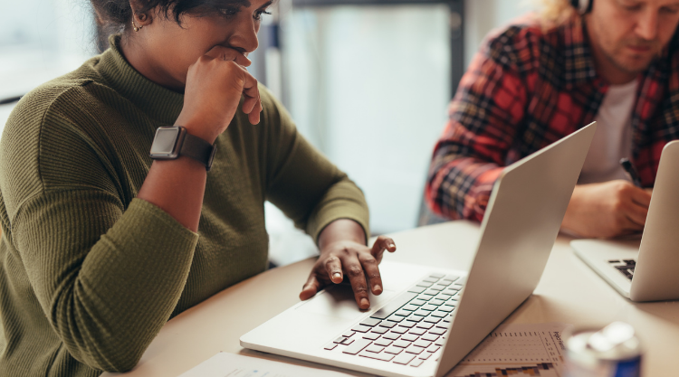 An adult woman typing on her laptop next to an adult man wearing headphones and working on his laptop