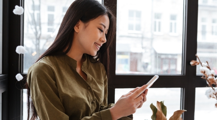 A young woman looks down at her cell phone while seated in a cafe