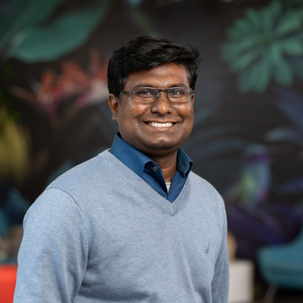 Headshot of a smiling adult man standing in front of a floral mural