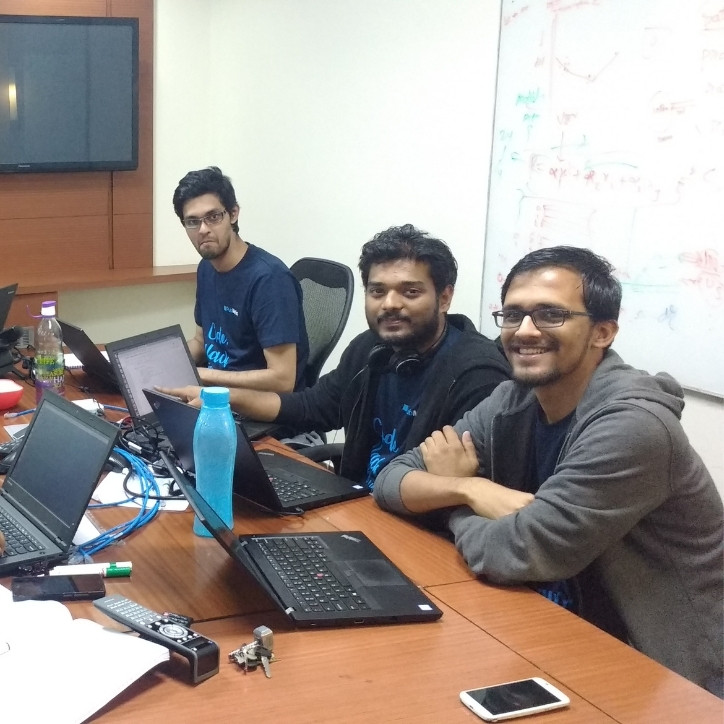 Three adult men with four laptops open and working in an office