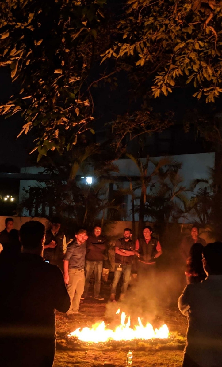 A crowd of PubMatic employees out in a field with a fire burning in front of them.