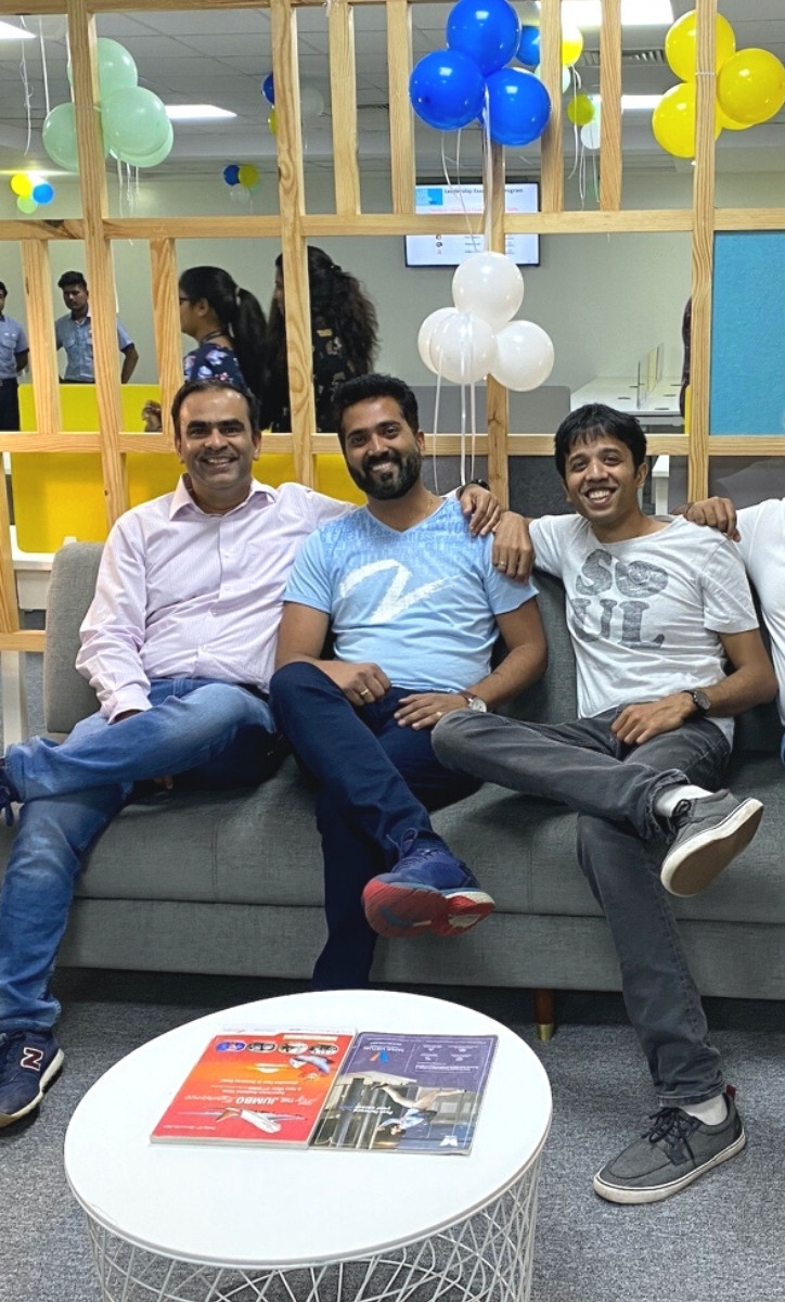 Three smiling adult sitting on a couch with several balloons behind them