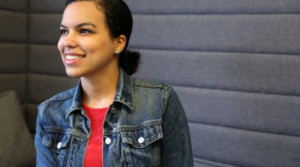 A smiling young woman looking forward and seated on a couch