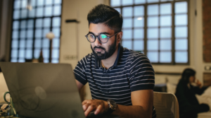 Student woking on his laptop in a library with a blurred out woman behind him