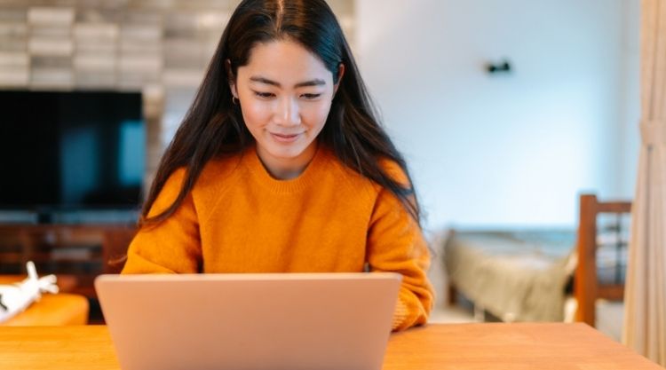 A smiling adult woman typing on her laptop in her house.