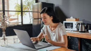 Smiling adult woman sitting in her kitchen working on her laptop