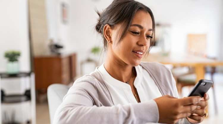 Woman sitting on couch at home, smiling at phone