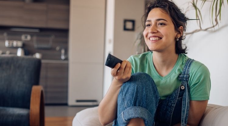 Woman lounging on couch at home holding TV remote