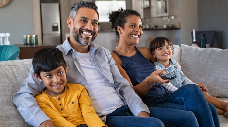 Happy young south asian family on couch watching tv