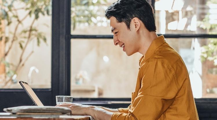 Happy young man in yellow shirt working on laptop