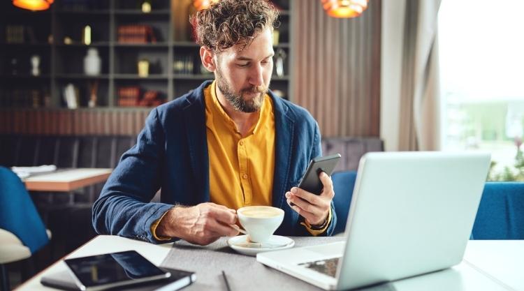 Man in a yellow shirt working in cafe with a laptop looking at phone