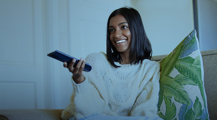 Shot of a young woman holding a remote control while sitting on the couch at home