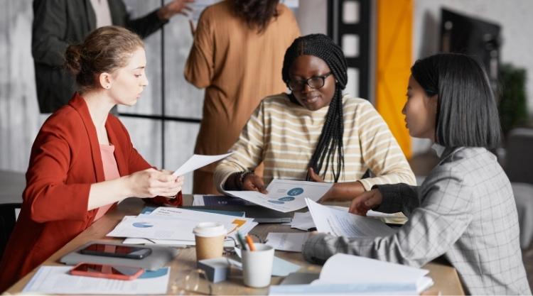 A group of smiling multicultural women sitting at a table while working.
