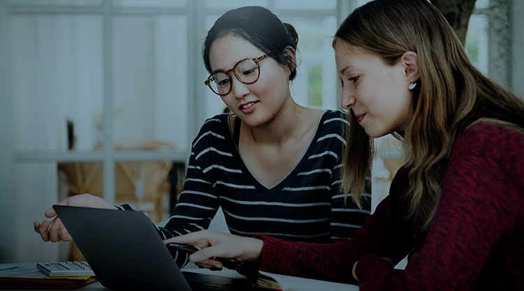 Two women looking at the computer screen with books on desk