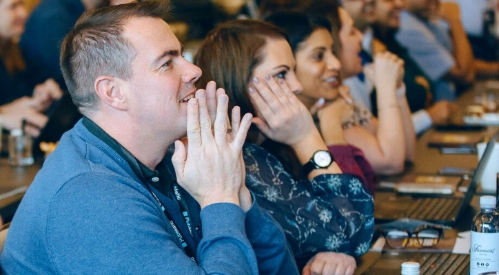A crowd of adults in a conference are cheering as they listen to the presentation