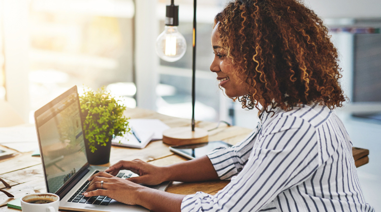 Cropped shot of a woman using her laptop on a wooden table
