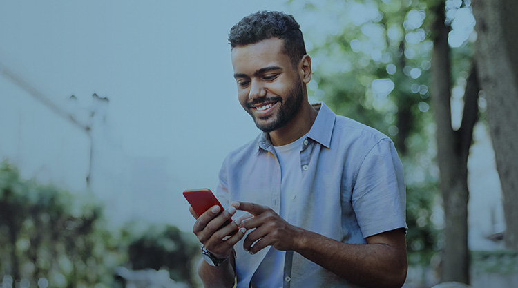 Cheerful young man using smart phone in a park