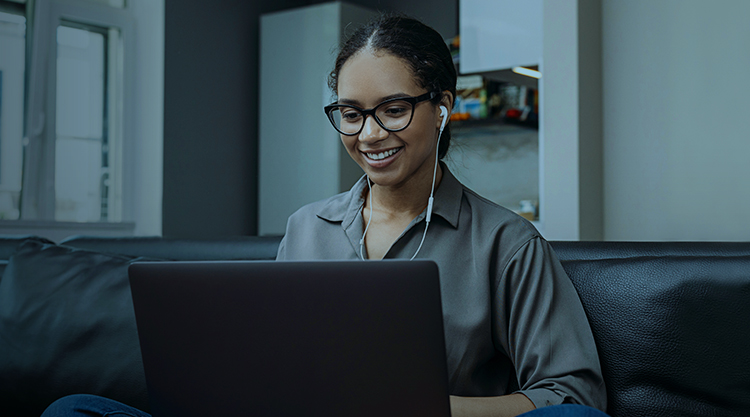 Young woman video calling using a laptop sitting on a sofa wearing earphones