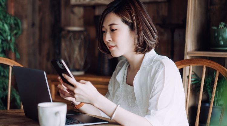 A content young woman uses her mobile device while her coffee cools