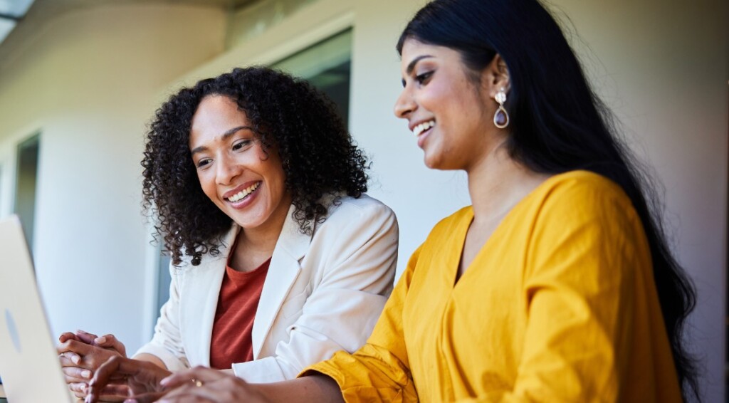 Two businesswomen smiling and working on a laptop at an office table